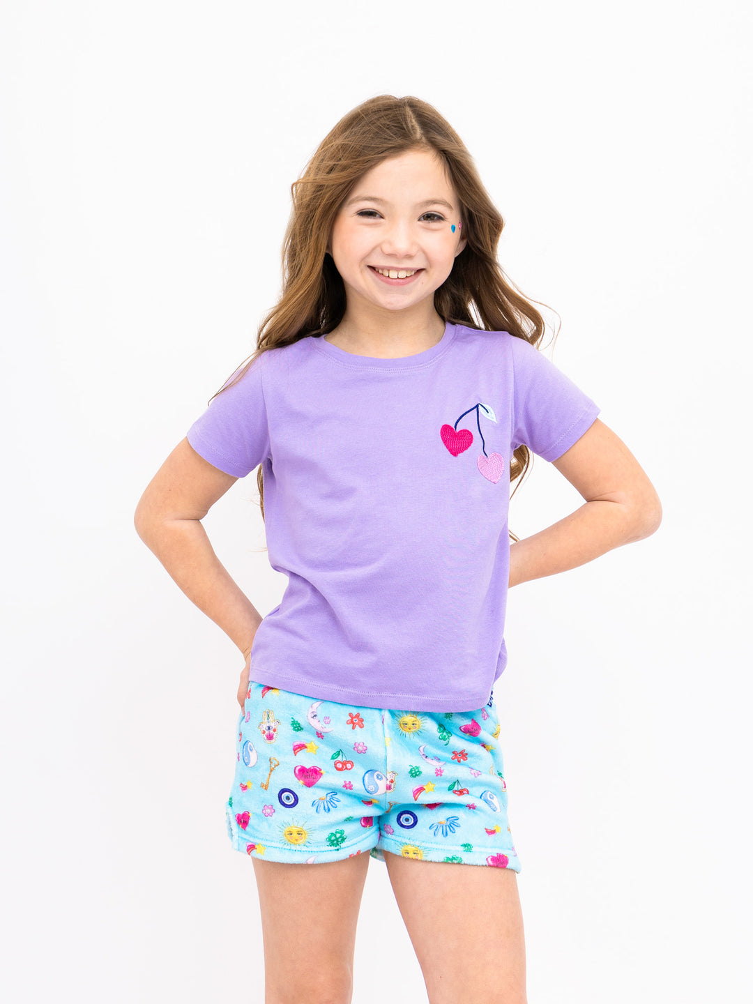 Young girl wearing a purple shirt and light blue shorts with lucky charm print on a white background