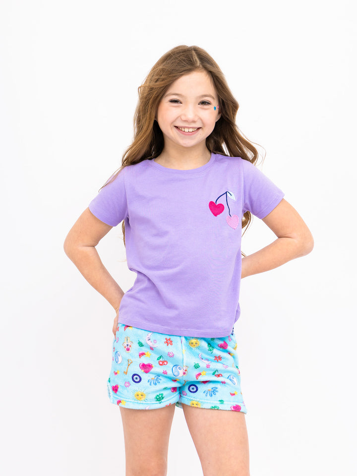 Young girl wearing a purple shirt and light blue shorts with lucky charm print on a white background