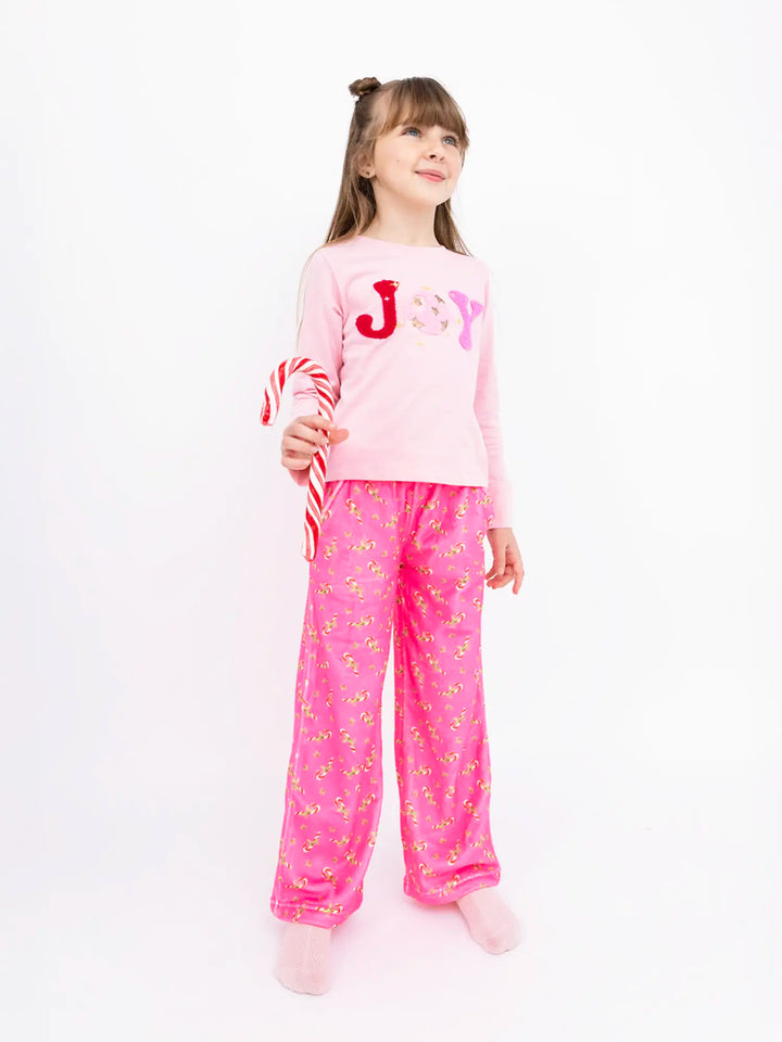 Child wearing pink candy cane pluhs lounge pants and shirt with 'JOY' on a white background