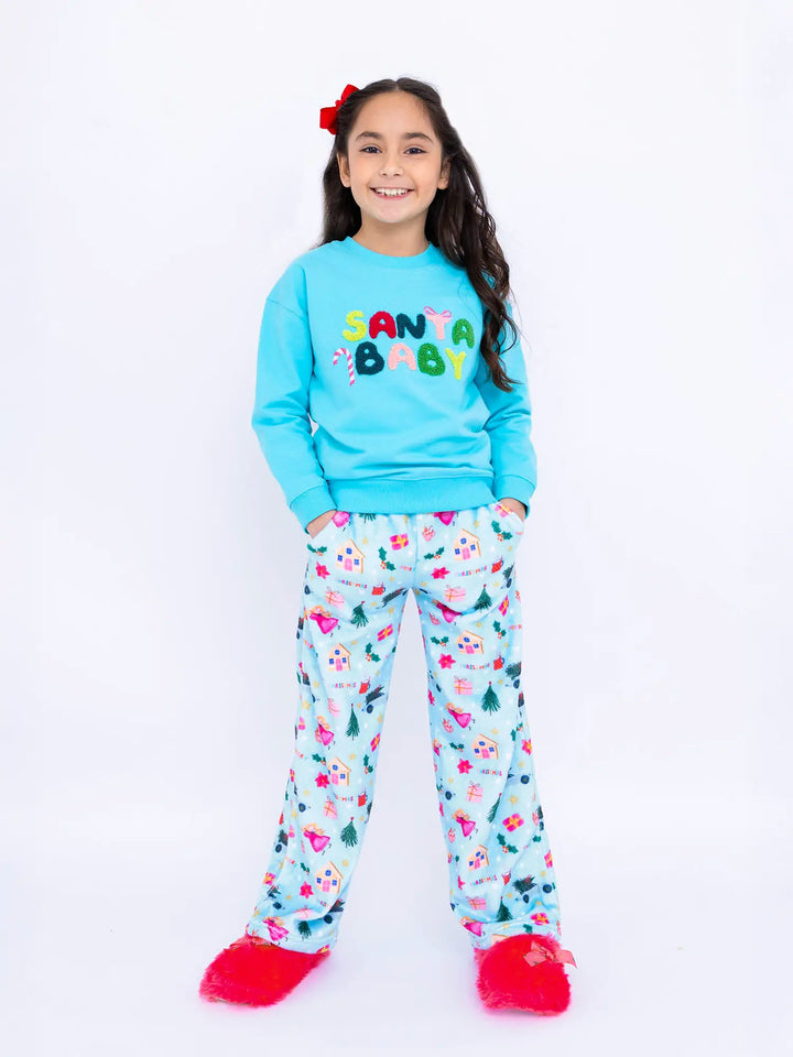 Girl wearing a 'Santa Baby' sweatshirt and chirstmas print plush pants on a white background