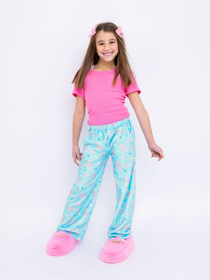 Young girl wearing a pink shirt and blue hanukkah printed plush pants on a white background