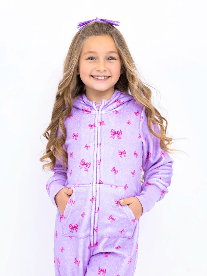 Young girl wearing a purple onesie with pink bows on a white background