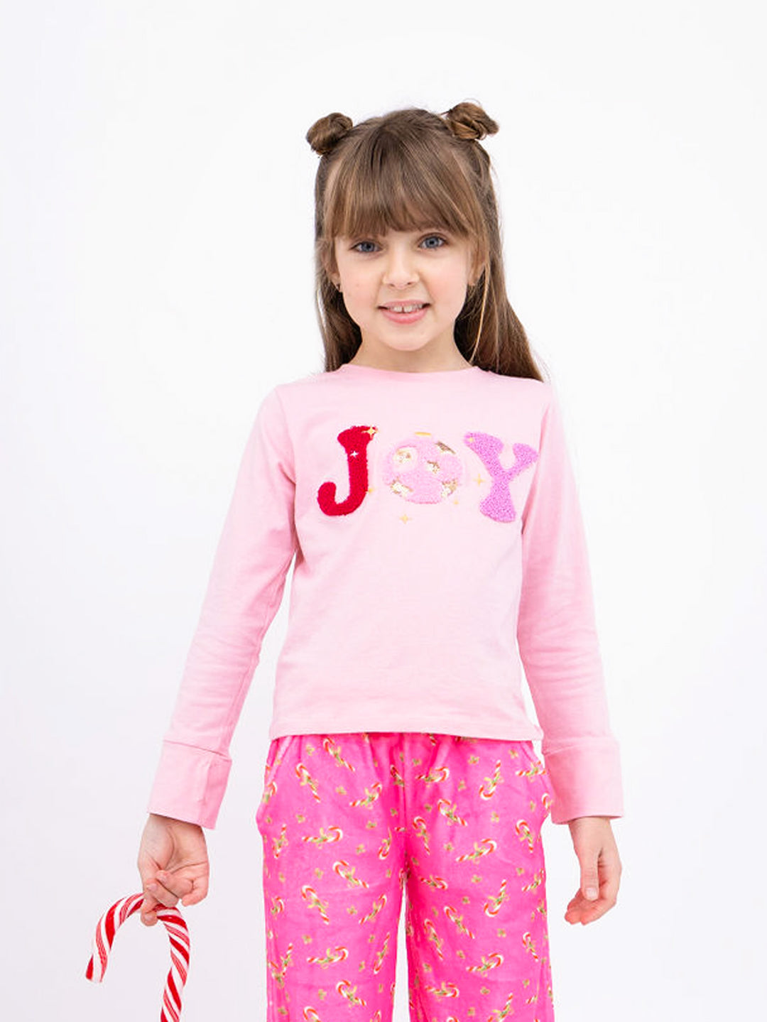 Young girl wearing a pink 'JOY' outfit with candy canes on a white background