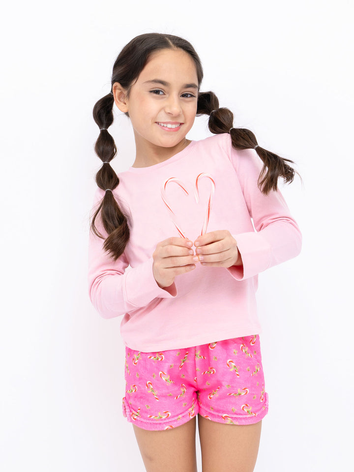 Young girl wearing a pink outfit with plush candy cane shorts on a white background