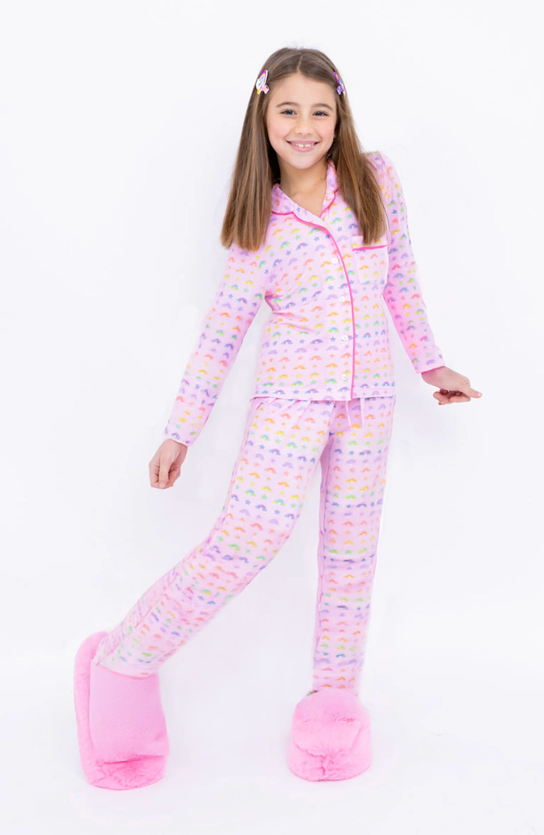 Young girl wearing a pink rainbow printed pajama set on a white background