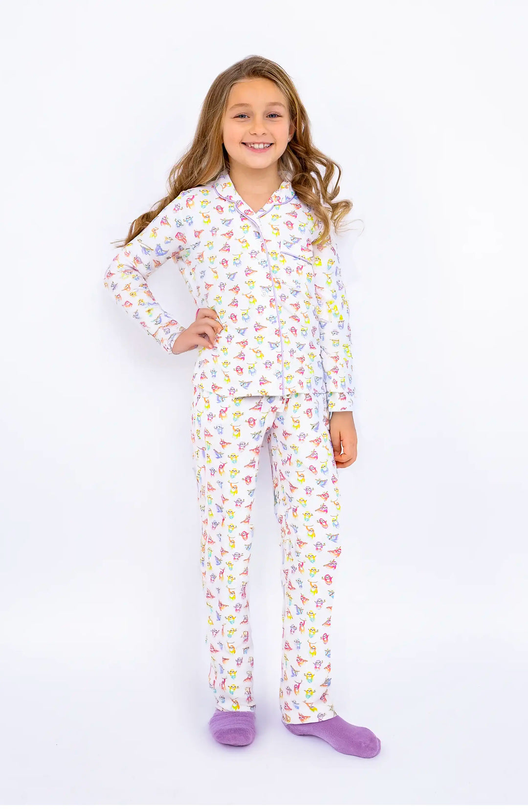 Young girl wearing a colorful sloth printed pajama set on a white background