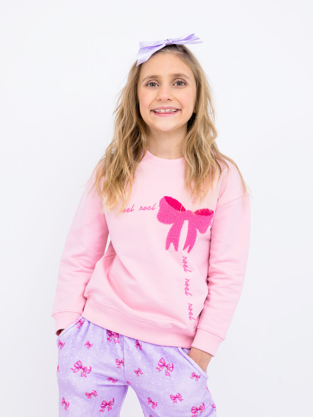 Young girl wearing a pink sweatshirt with a bow design and matching pajama pants on a white background