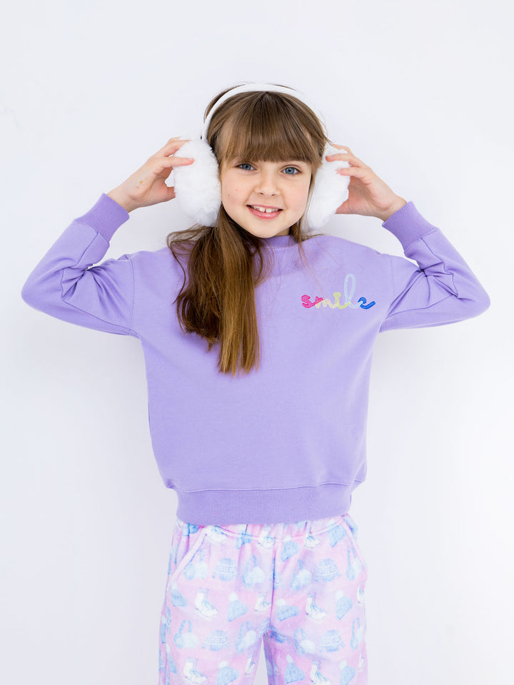 Child wearing a purple sweatshirt with 'smile' text and colorful pants on a white background