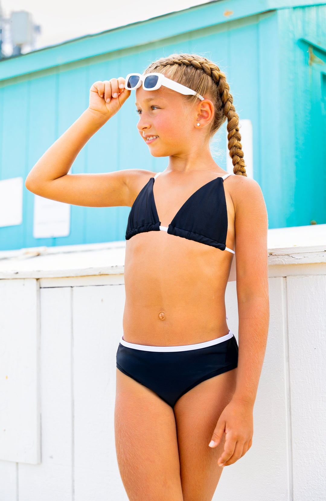 Young girl in a black string bikini with sunglasses on a beach.