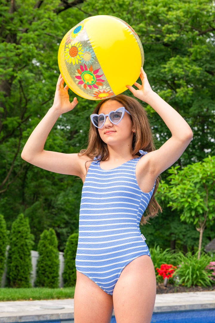 girl in a blue striped one piece swimsuit holding a colorful beach ball outdoors.