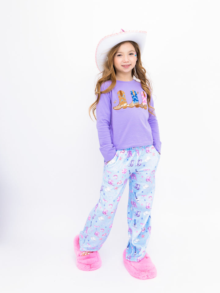 Young girl wearing a purple top and light blue plush pants with pink slippers on a white background
